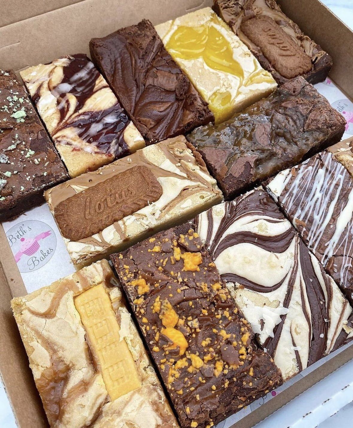 An assortment of gourmet brownies with various toppings and flavors, presented in a box from Beth's Bakes.