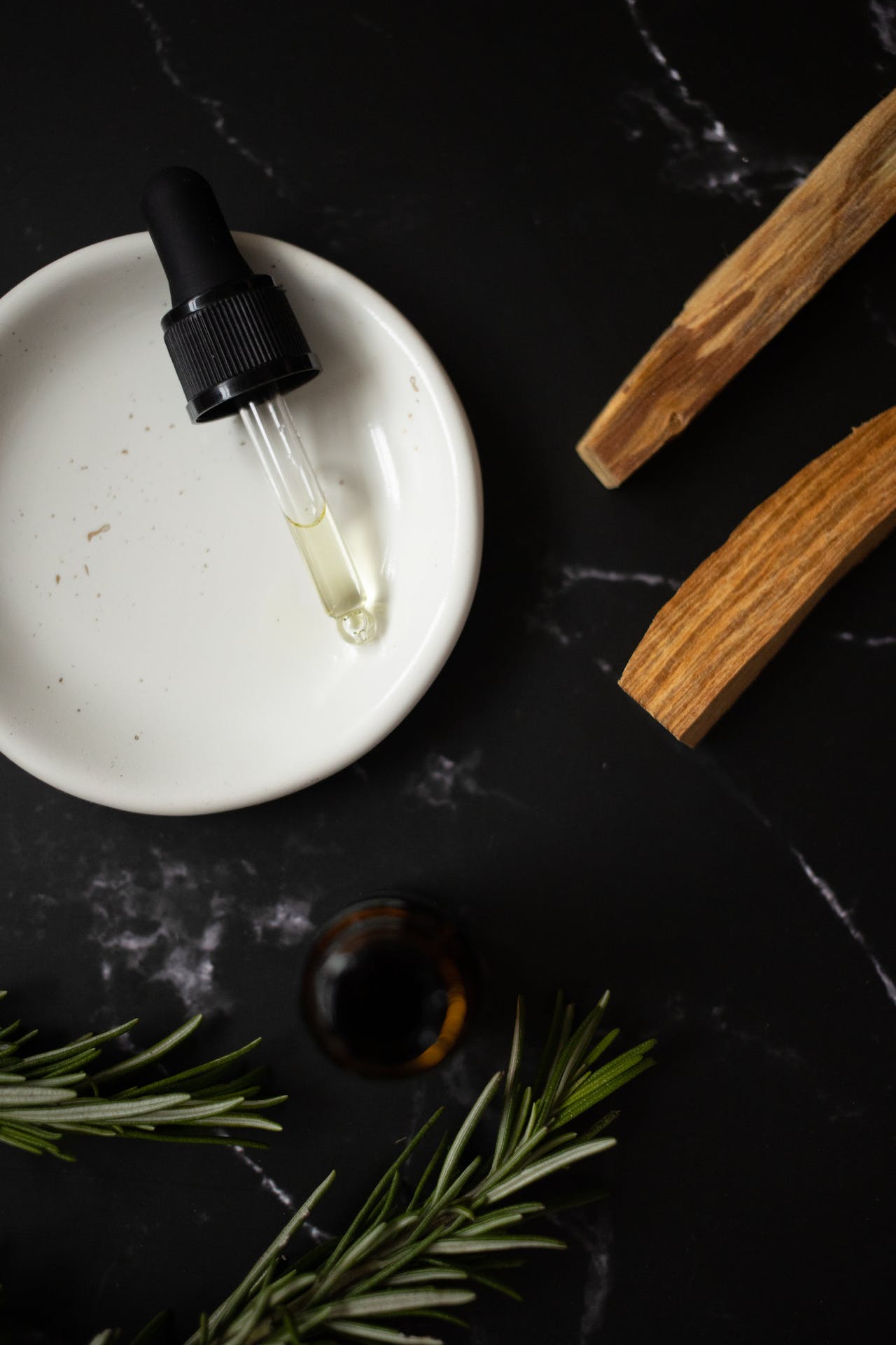 A white plate with a bottle of essential oil and sprigs of rosemary.