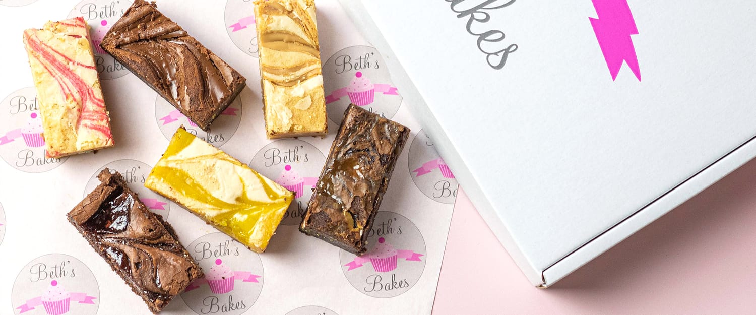 Assorted brownies and lemon bars displayed beside a pink bakery box with "Beth's Bakes" logo.