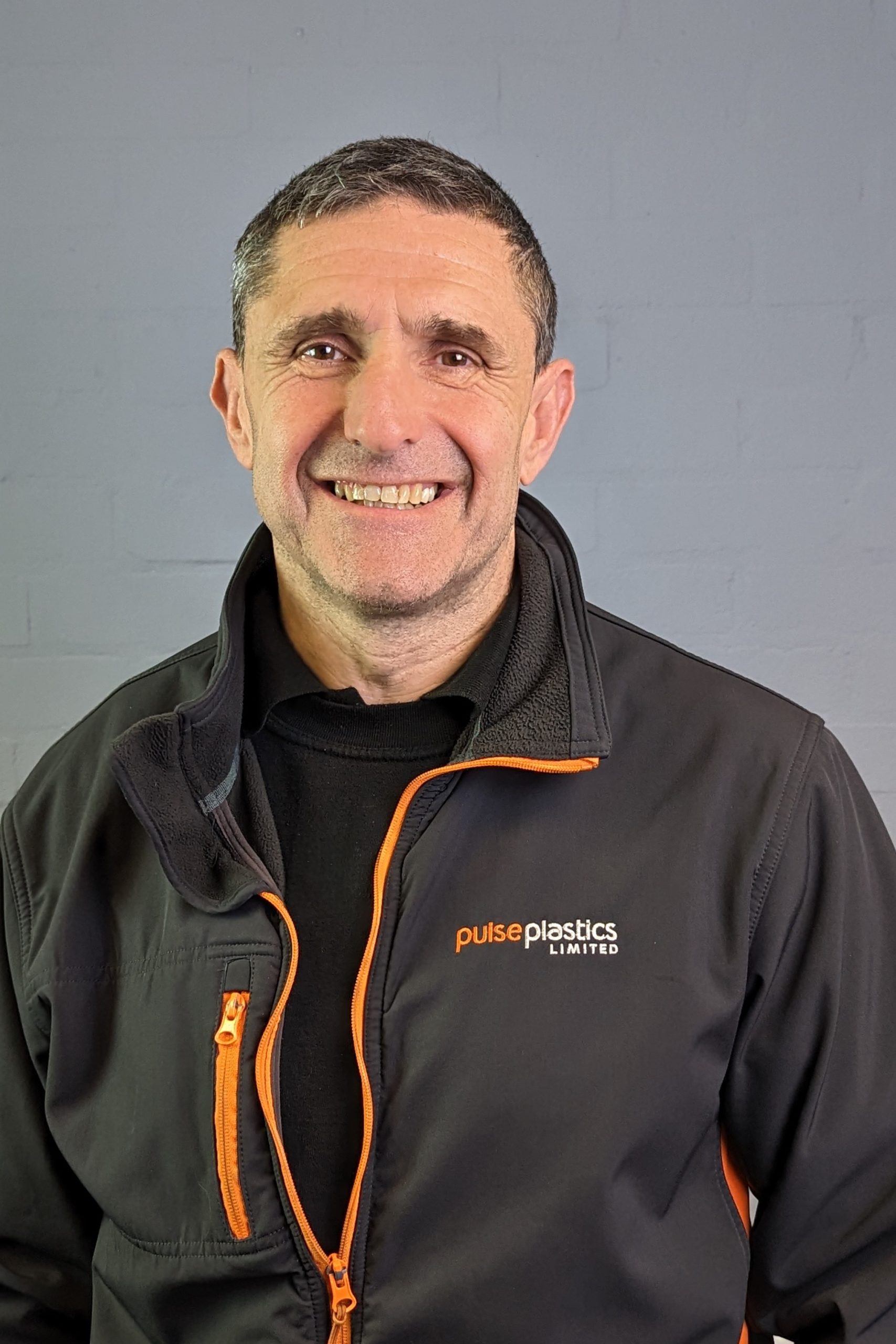 A Pulse Plastics employee in a black and orange jacket smiling.