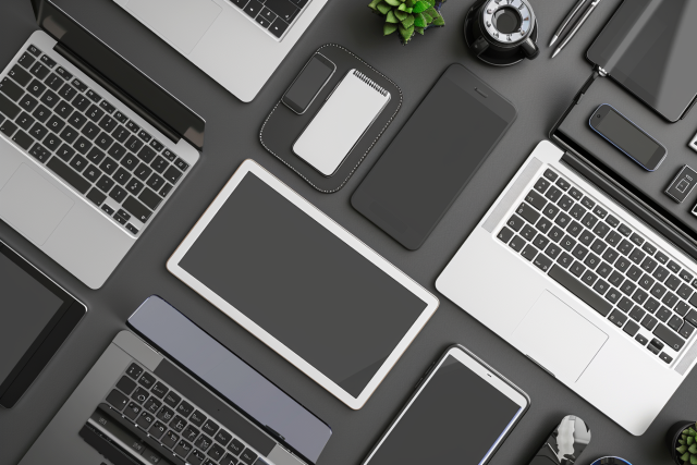 Top view of a modern workspace with multiple open laptops, a tablet, smartphones, and various gadgets organized on a grey surface for responsive web design.